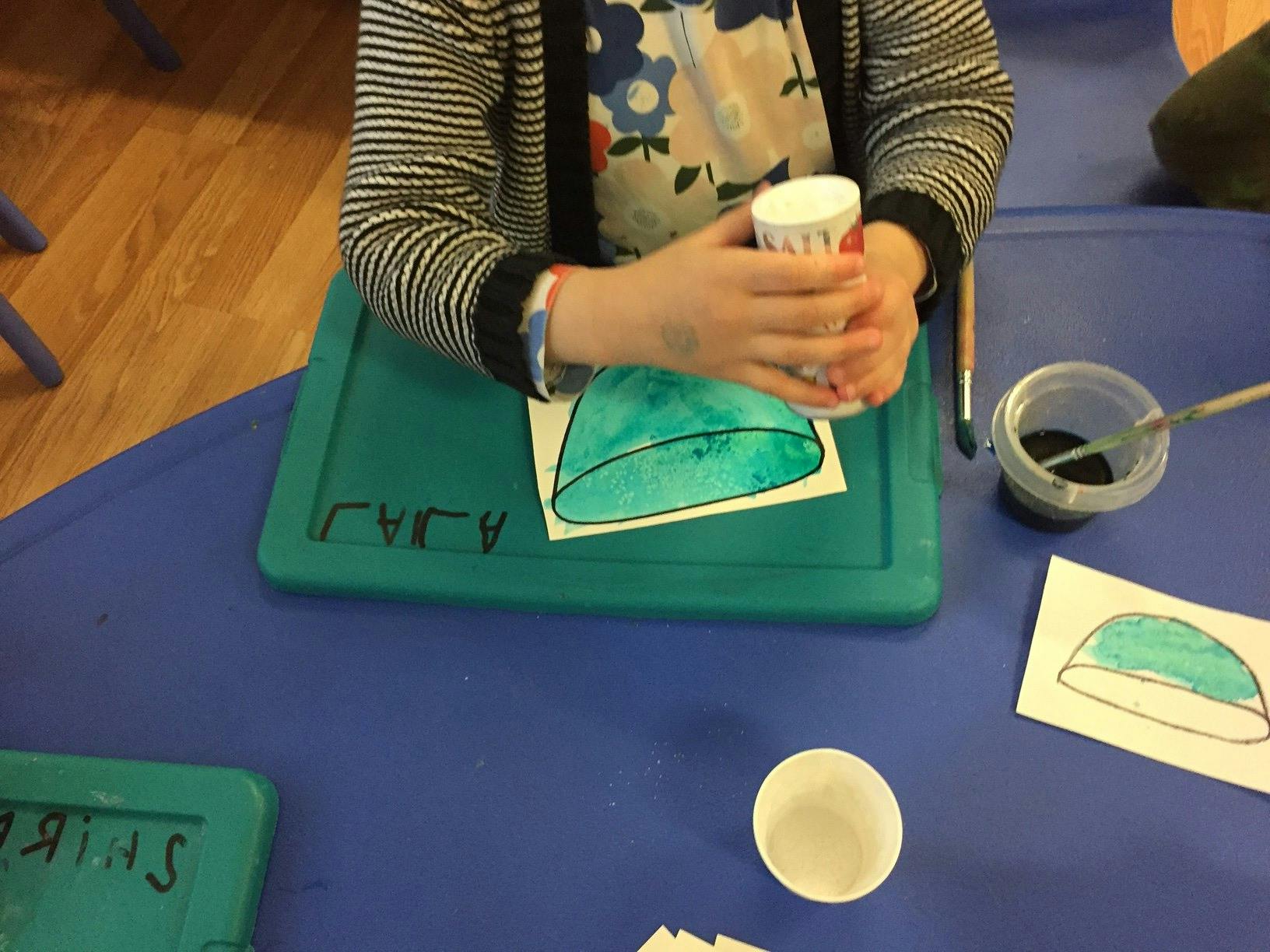 Child holding a cup over a drawing of a green shape