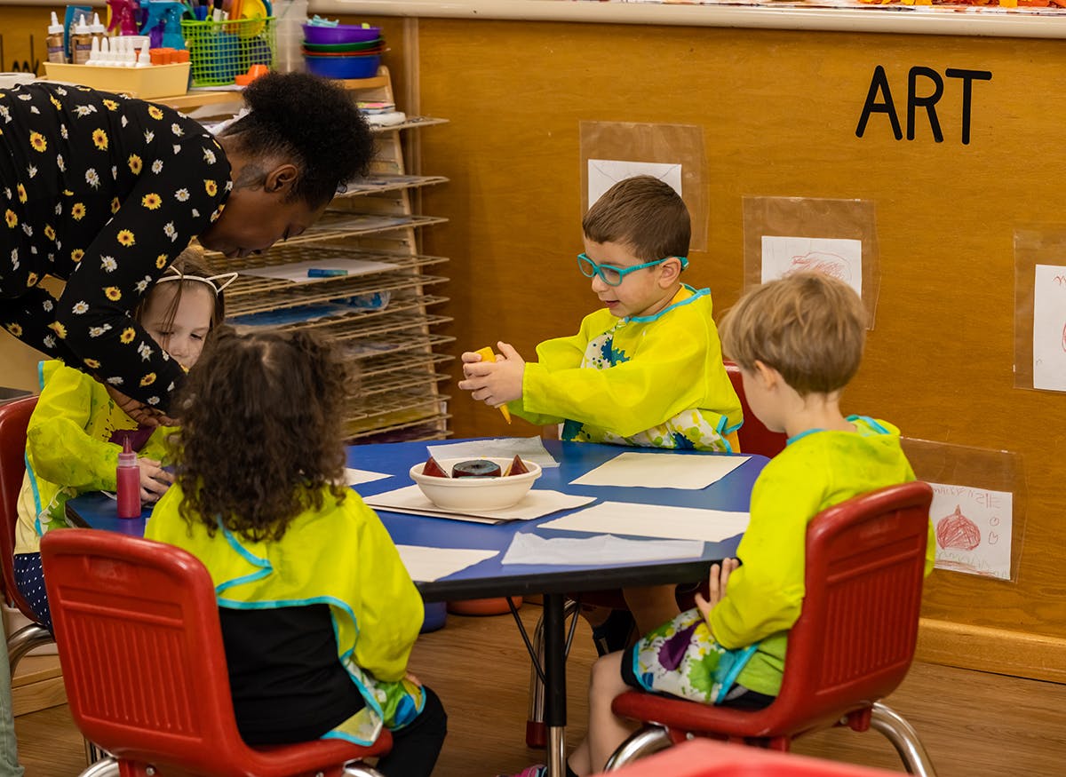 Person leaning over a table with children in a classroom