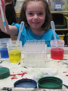 Child holding a pipette over beakers with colored liquid