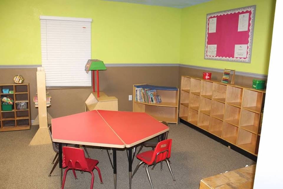 Classroom with red tables and chairs, shelves, and a bulletin board