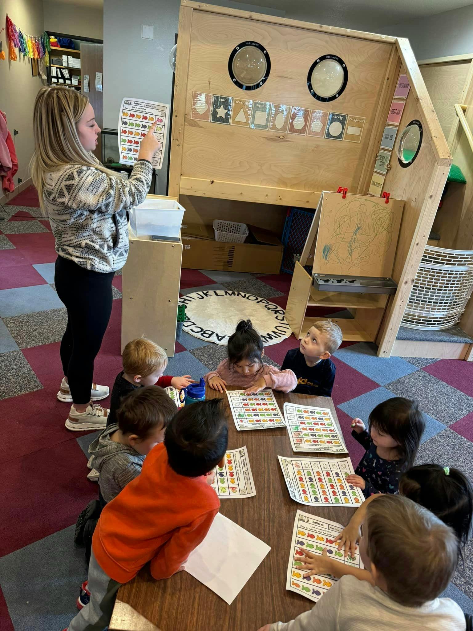 Person pointing to a chart while children sit at a table with papers