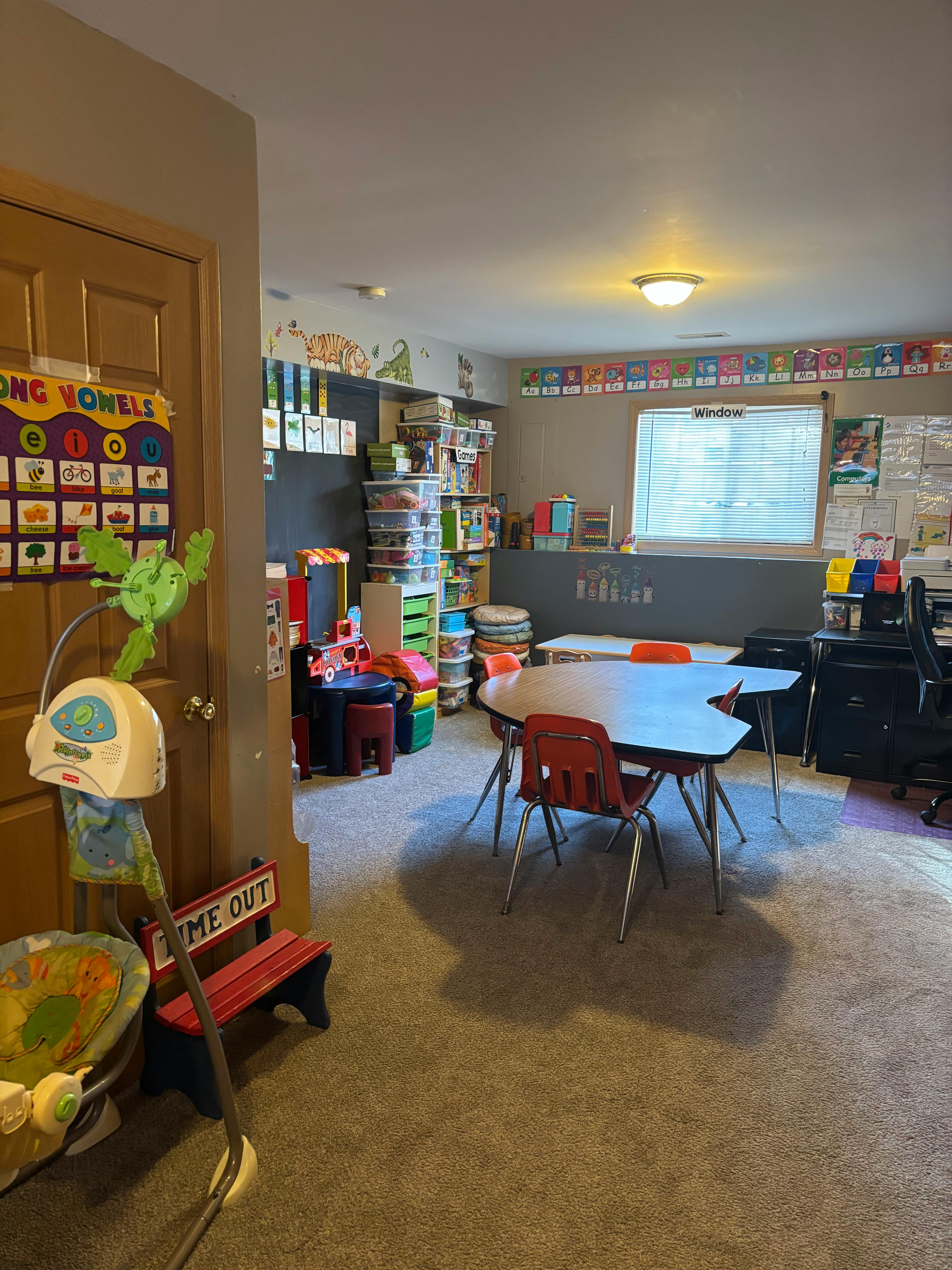 Classroom with small tables and chairs, shelves, and a "Long Vowels" chart