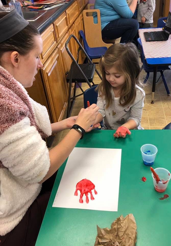 Person helping a child with red handprint art in a classroom