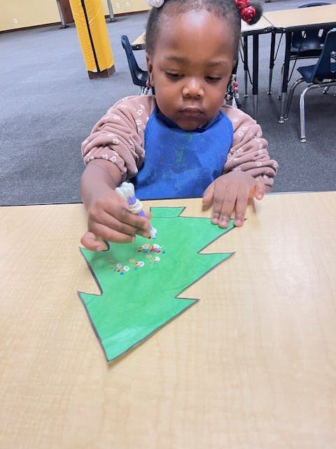 Child decorating a green paper tree with glitter glue