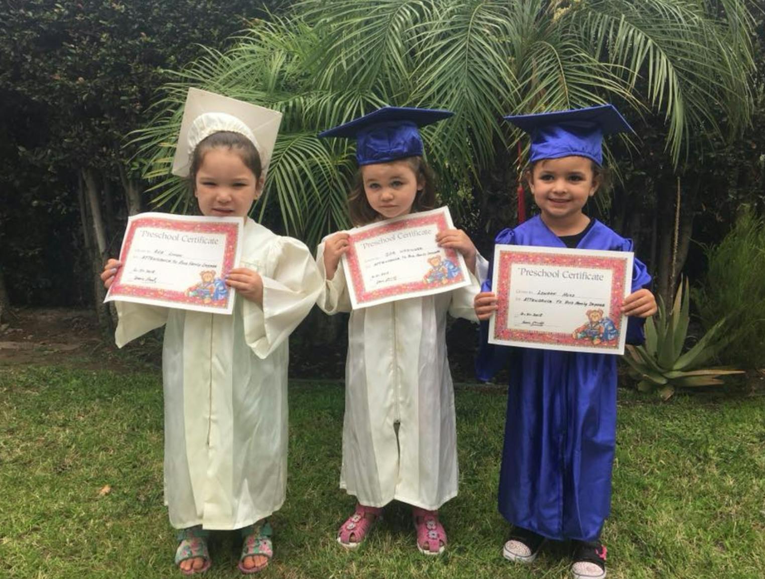 Three children in graduation caps and gowns holding certificates