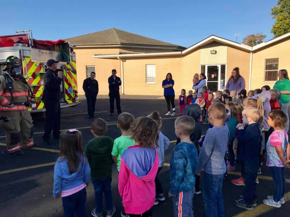 Firefighters and adults talking to a group of children outdoors