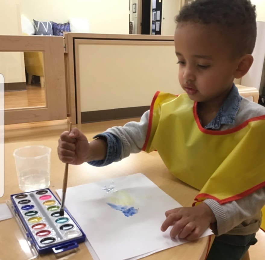 Child in a yellow smock painting with watercolors