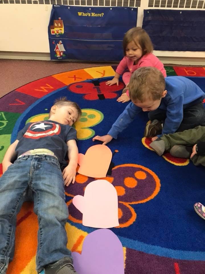 Three children on a colorful rug with mitten cutouts