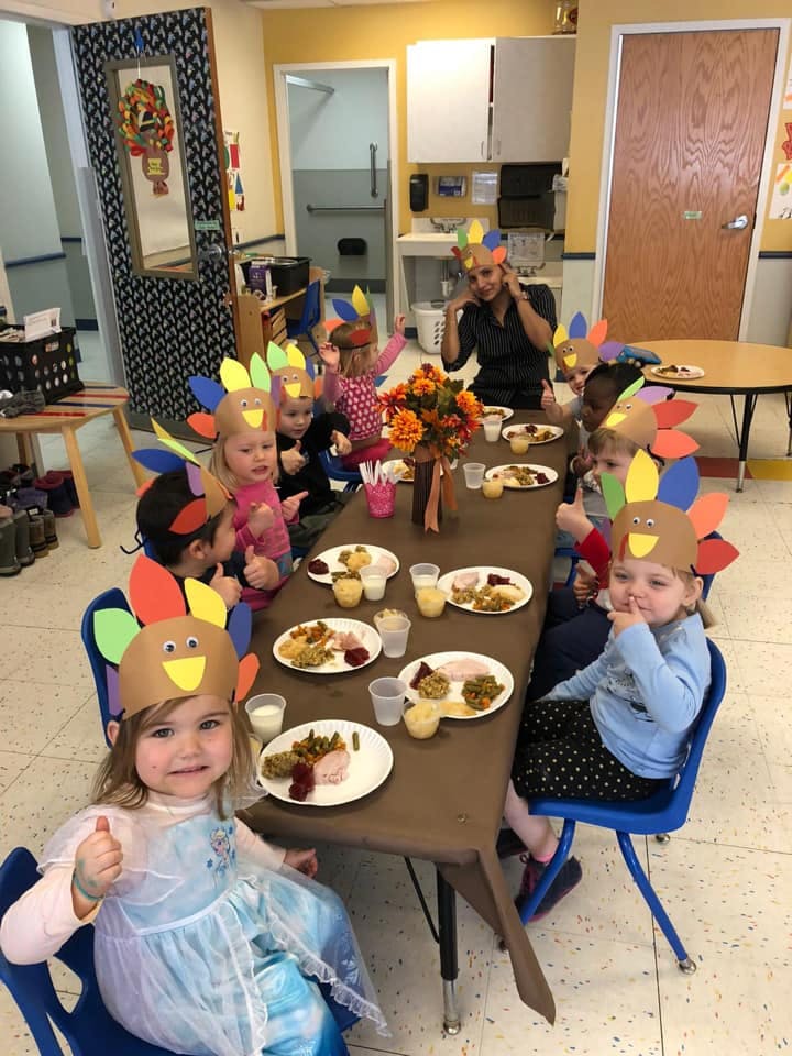 Children and an adult at a table with plates of food, wearing turkey headbands