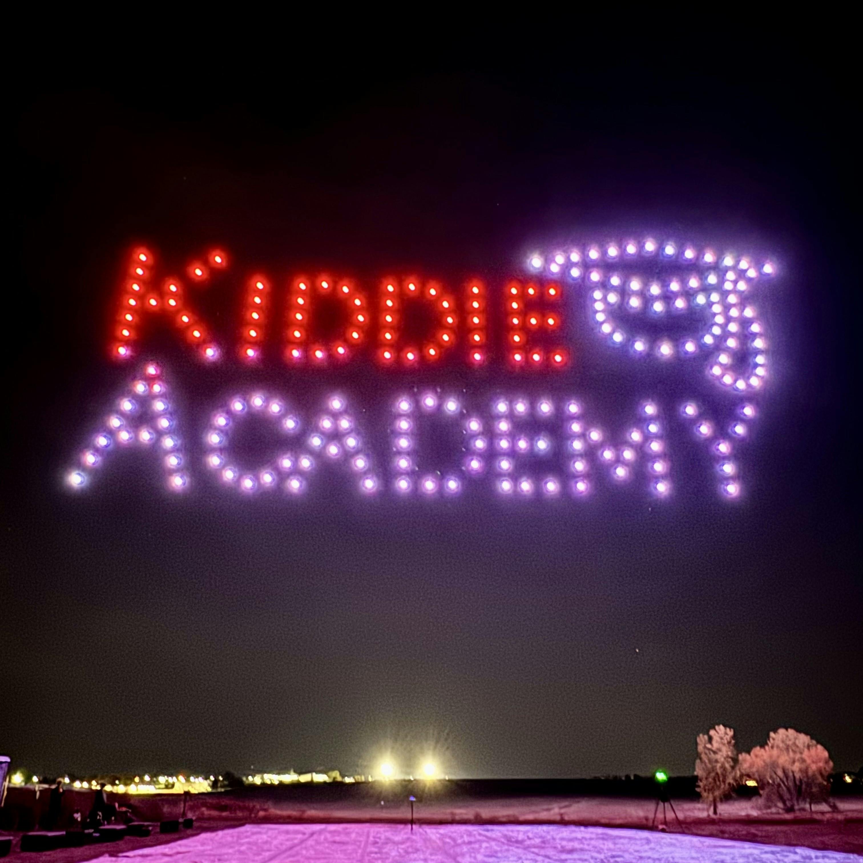 Drone light show spelling "KIDDIE ACADEMY" with a graduation cap