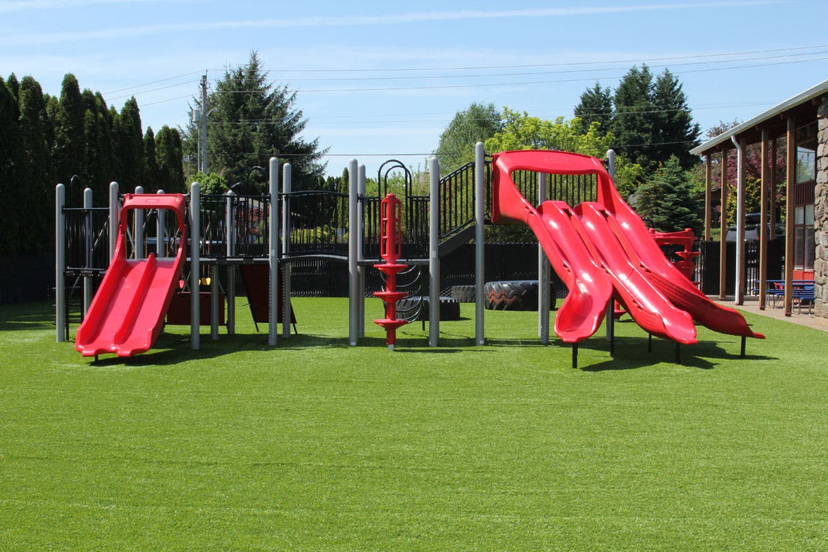 Red playground slides and climbing structure on green turf