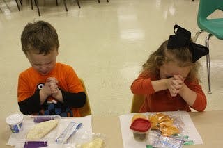 Two children with hands clasped, heads bowed at a table with food