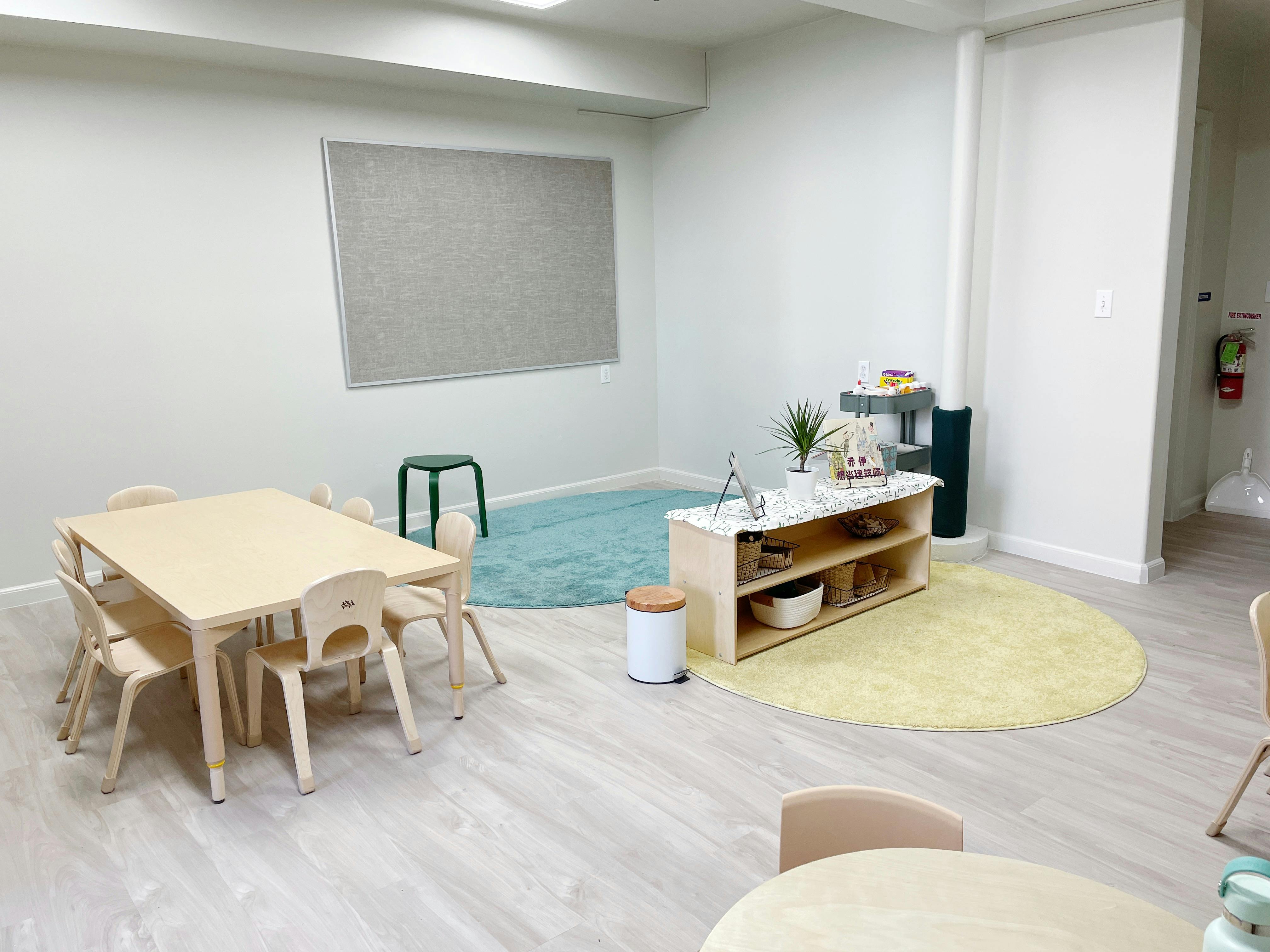 Classroom with small tables and chairs, a low shelf, and round rugs