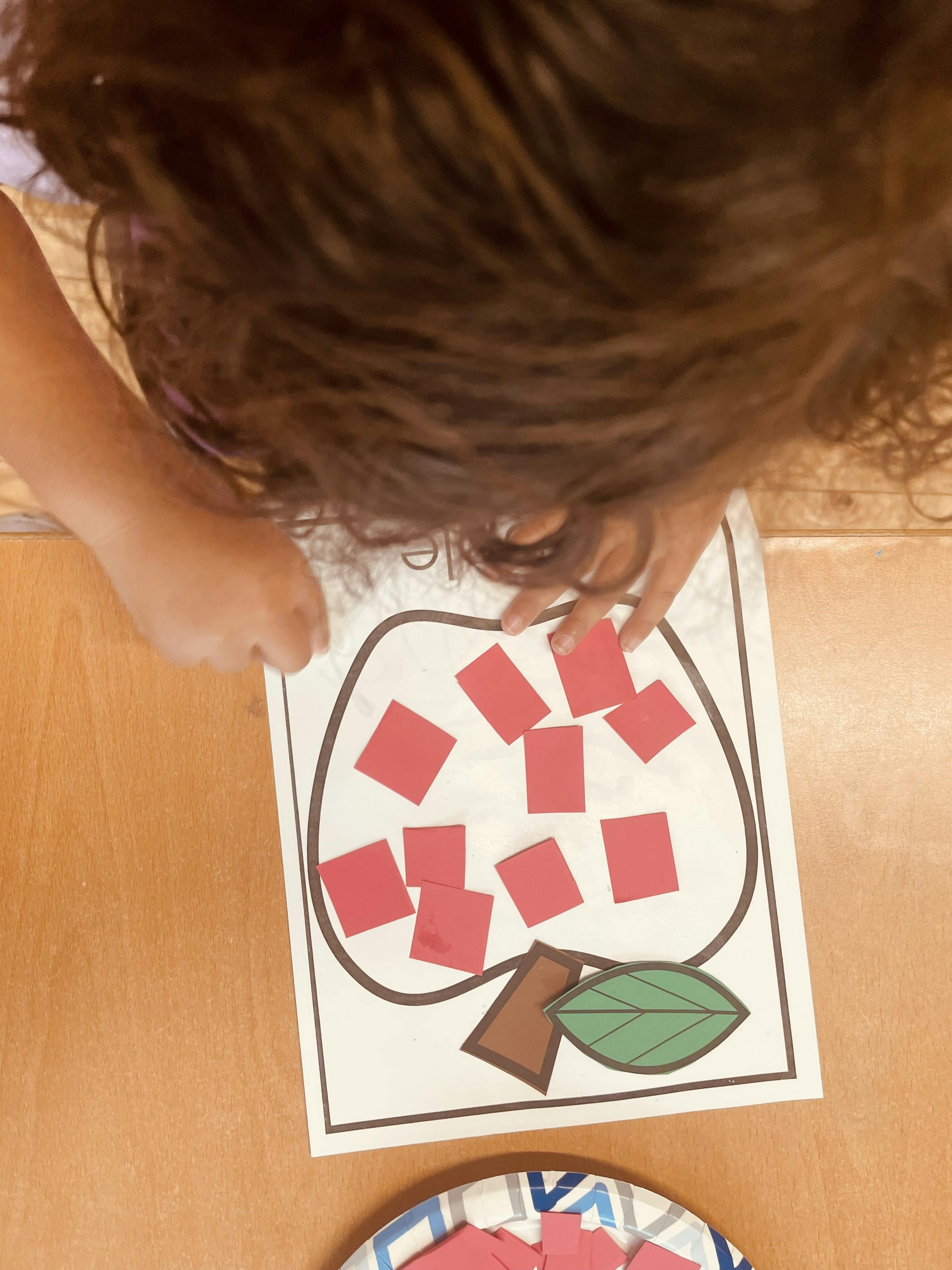 Child placing paper squares onto an apple-shaped worksheet