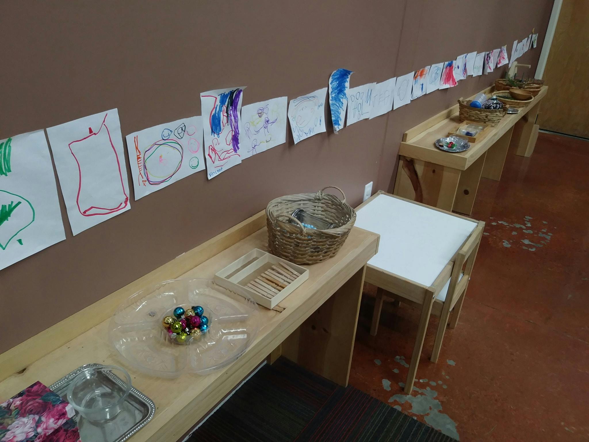 Children's drawings displayed on a wall above wooden tables with craft supplies