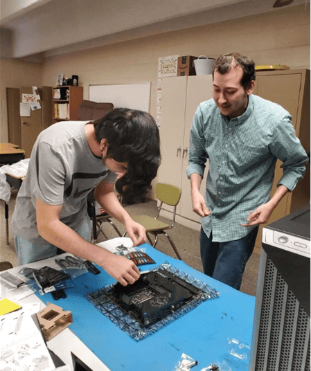 Two people assembling a computer motherboard in a classroom