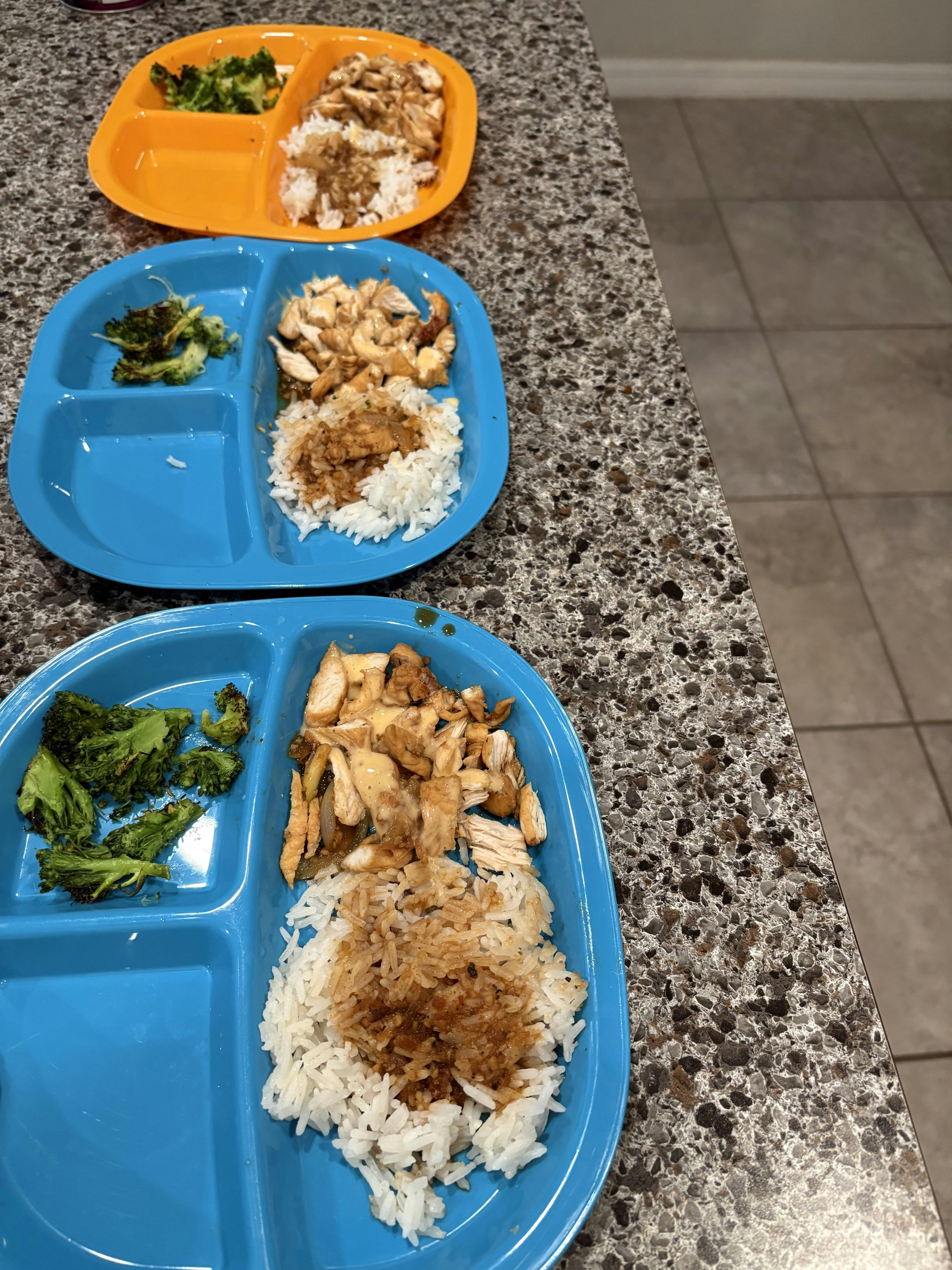 Three partitioned plates of chicken and rice with a side of broccoli
