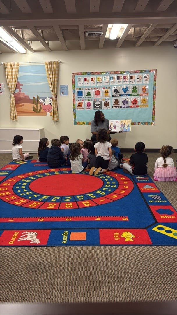 Teacher reading a book to a group of children sitting on a classroom rug