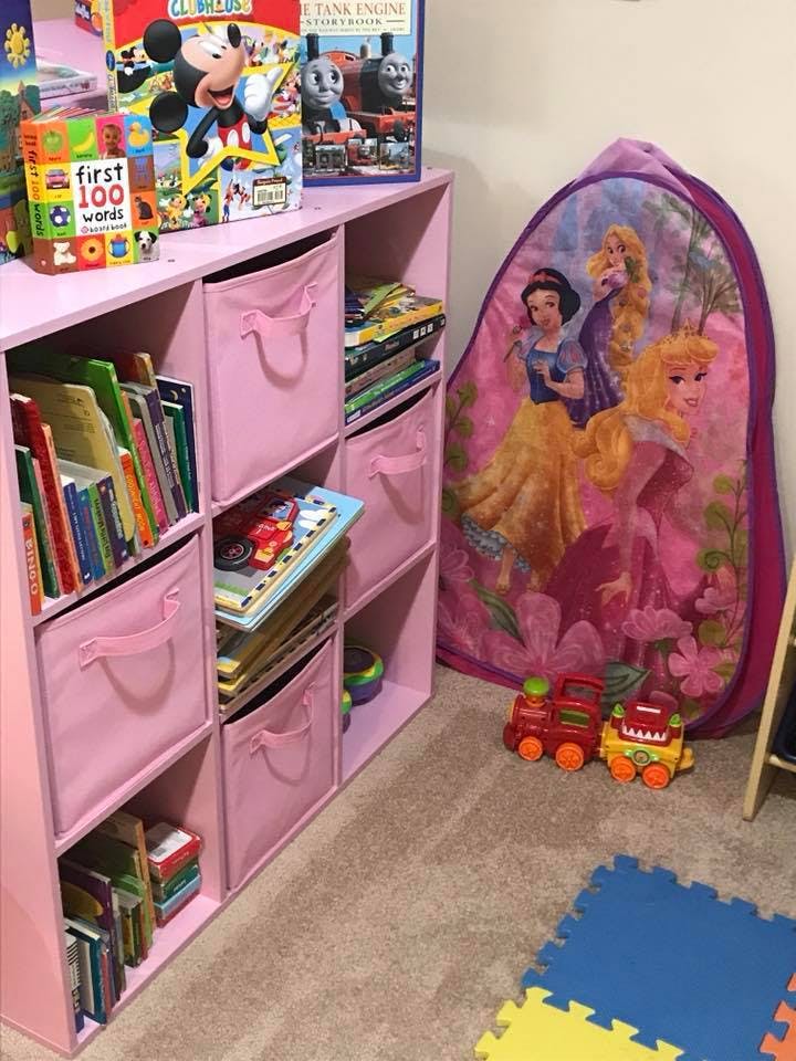 Pink storage shelves with books and toys, a playmat, and a princess tent