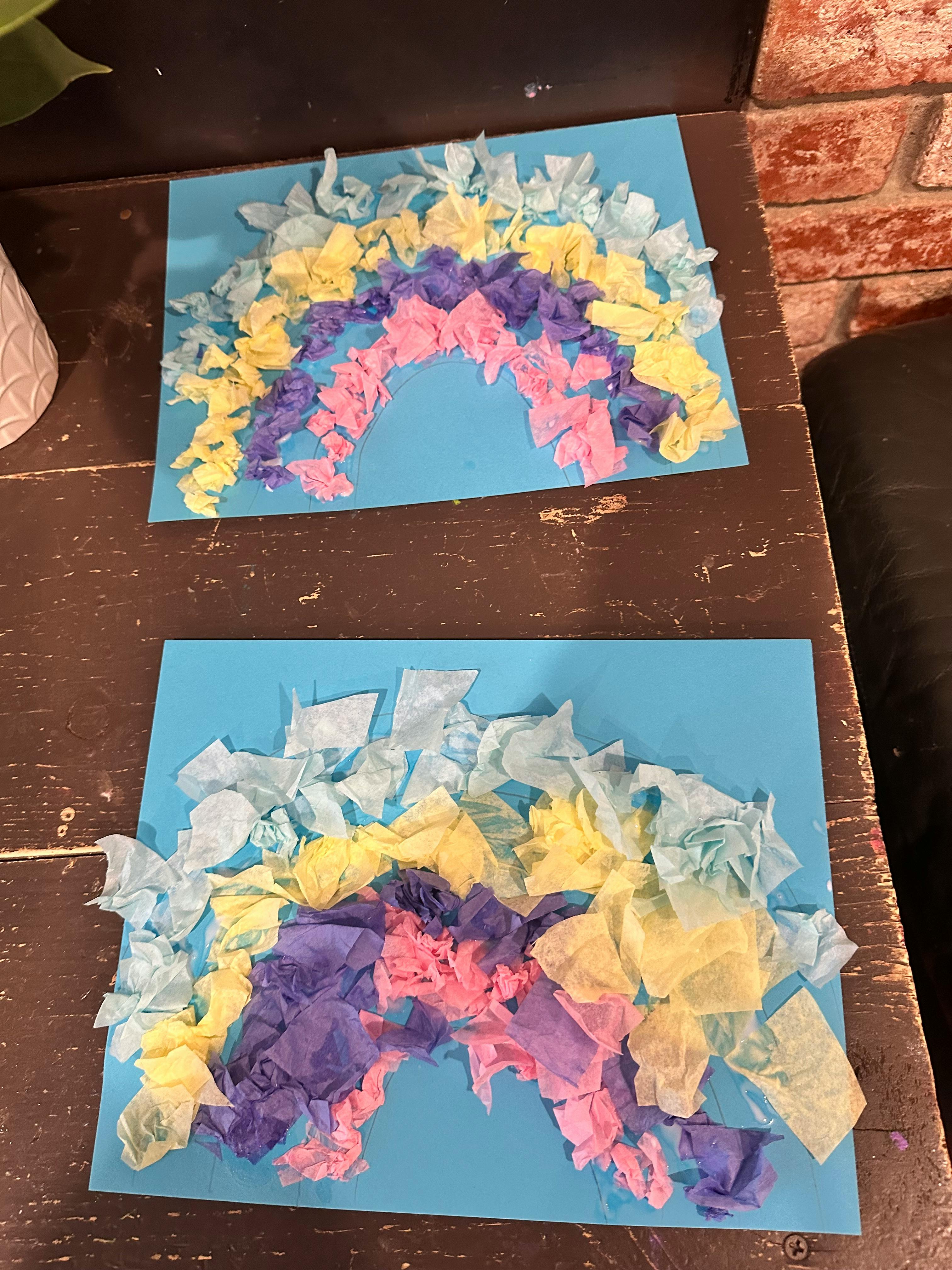 Two rainbow crafts made from crumpled tissue paper on blue paper