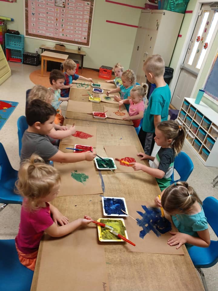 Children painting at a long table in a classroom