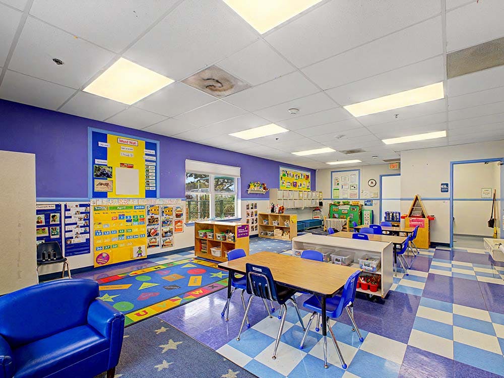 Empty children's classroom with small tables, chairs, and colorful decorations