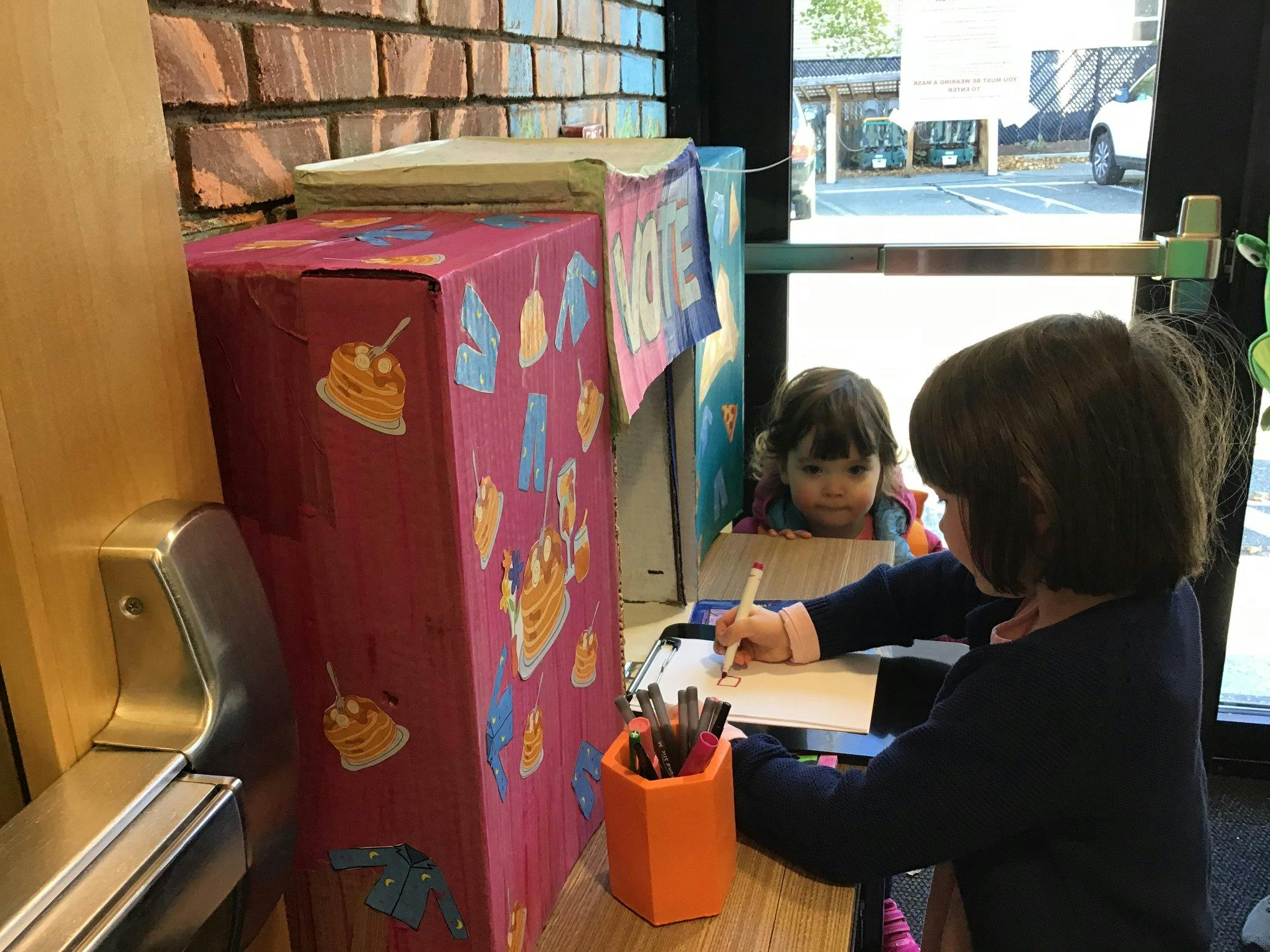 Child drawing at a table with another child looking on