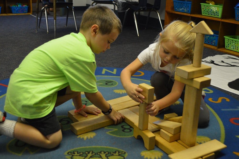 Two children building with wooden blocks on a rug
