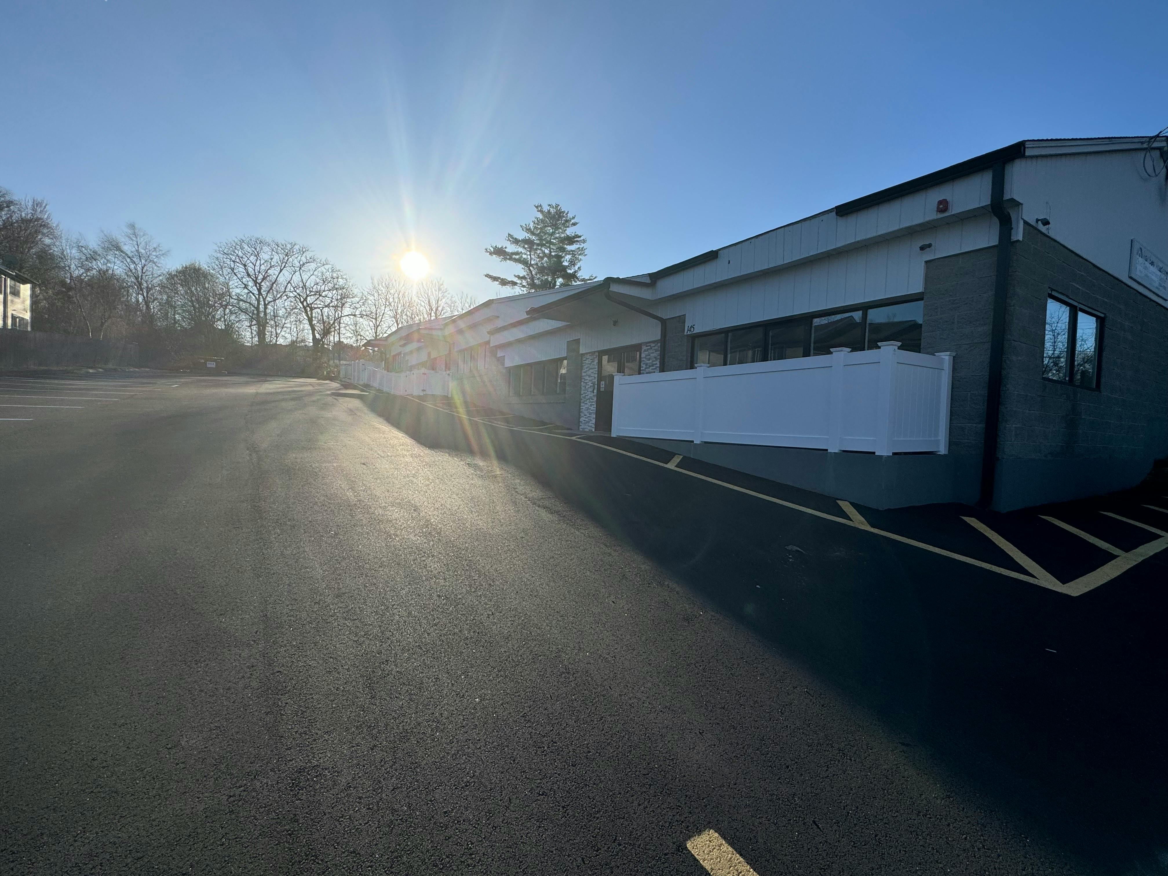 An empty parking lot next to a white and gray building under a bright sun