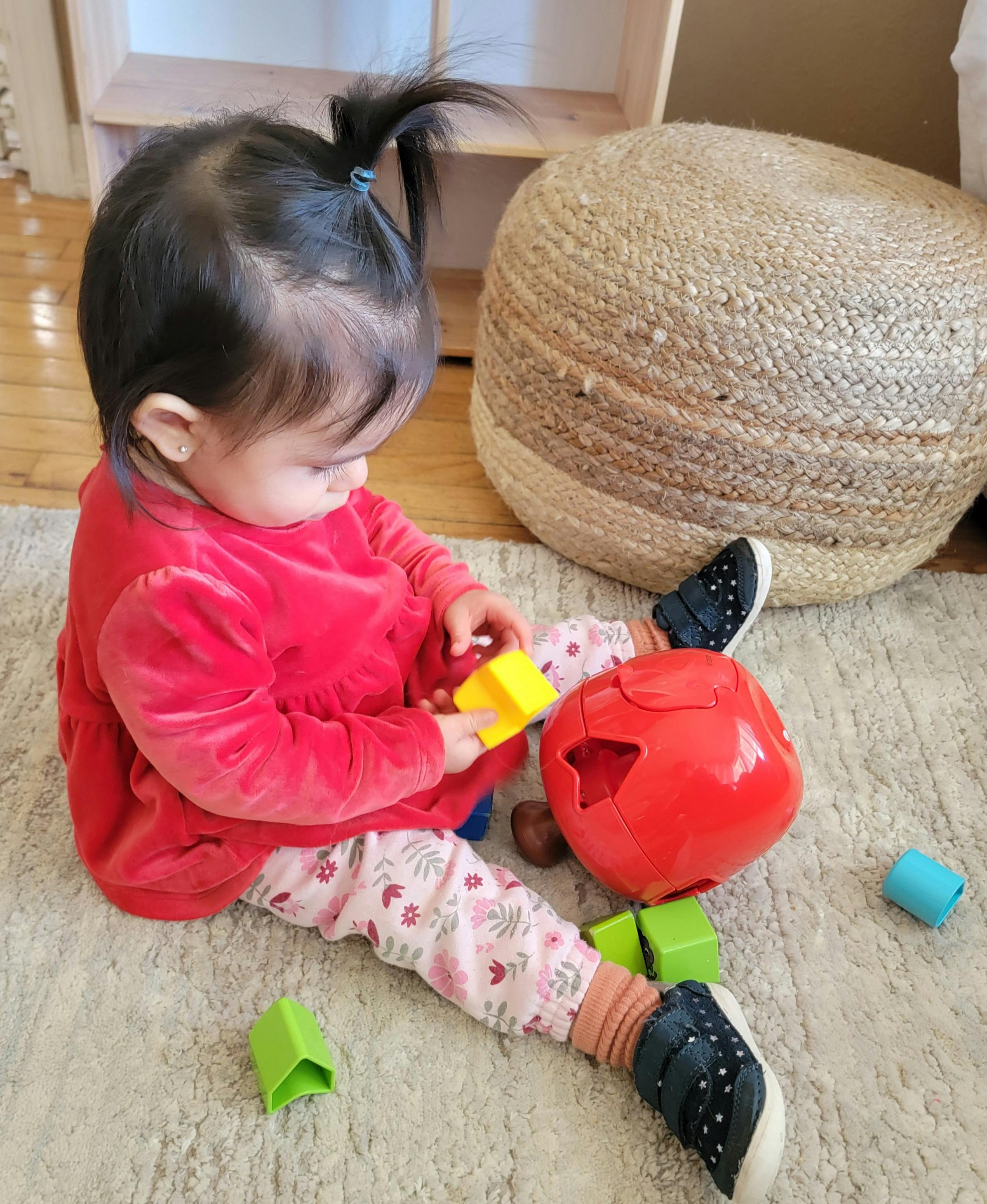 Child sitting on a rug playing with a red shape sorter and yellow block