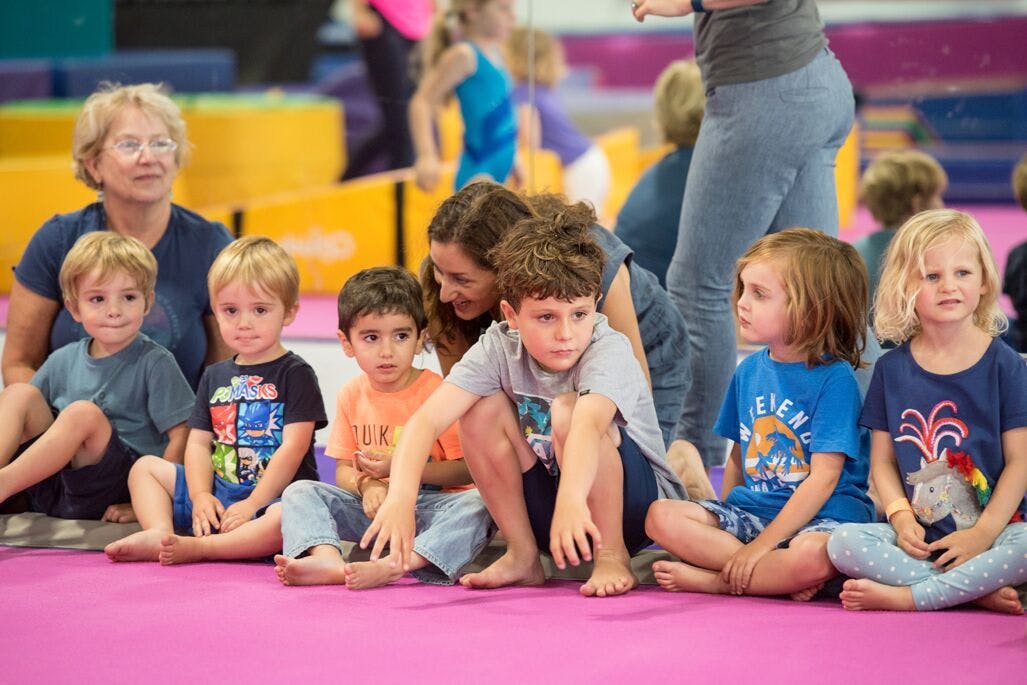 Adults and children sitting on a mat in a gym