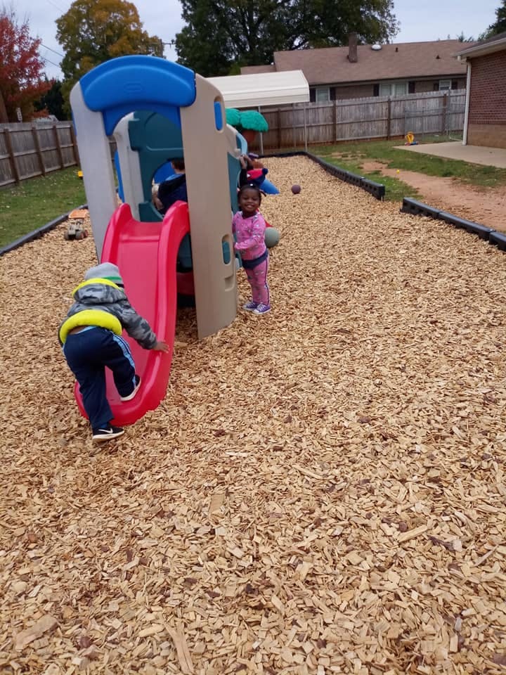 Child climbing onto a red slide on a playground, another child standing nearby