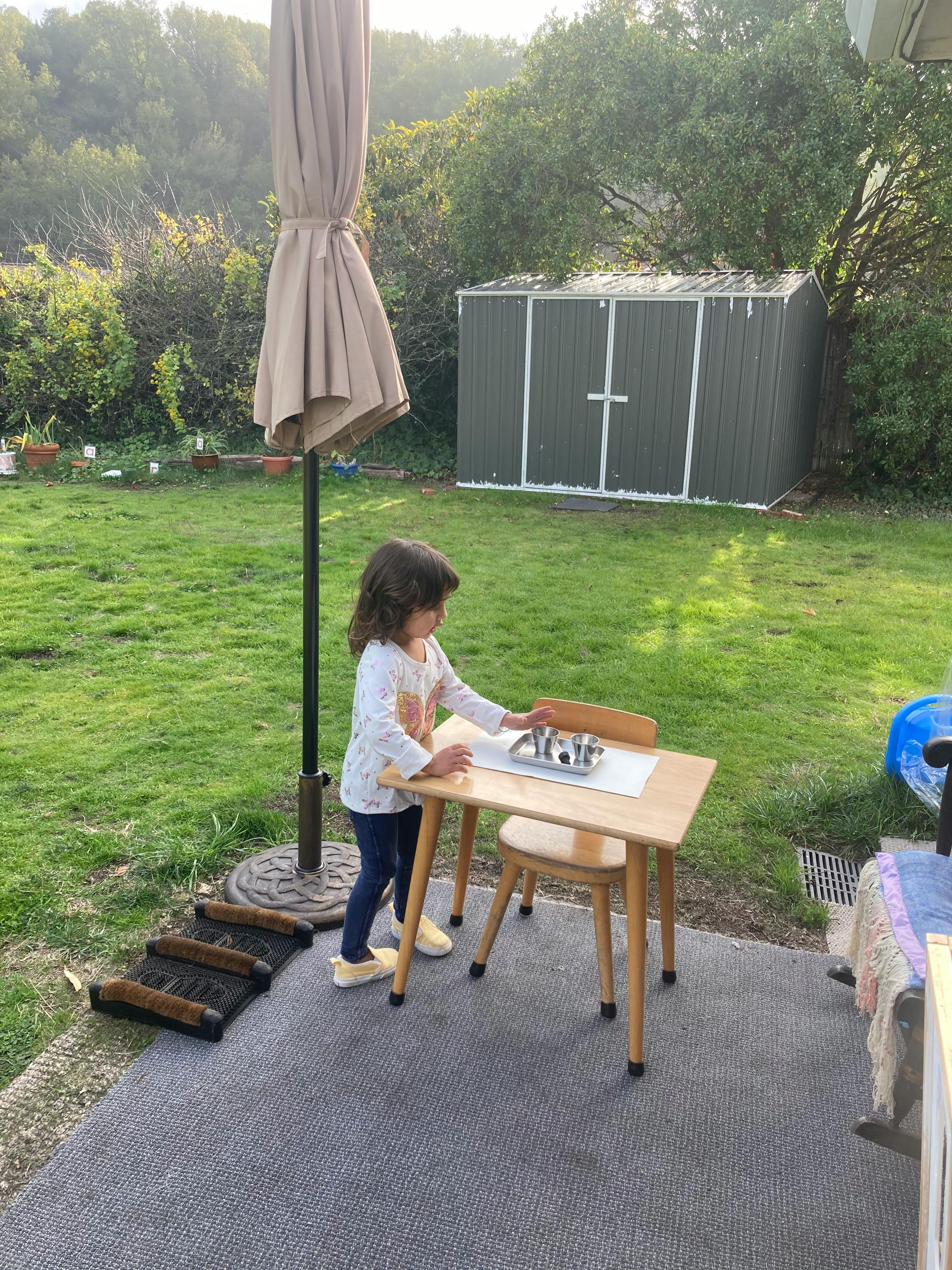 Child standing at a small table with a tray of items