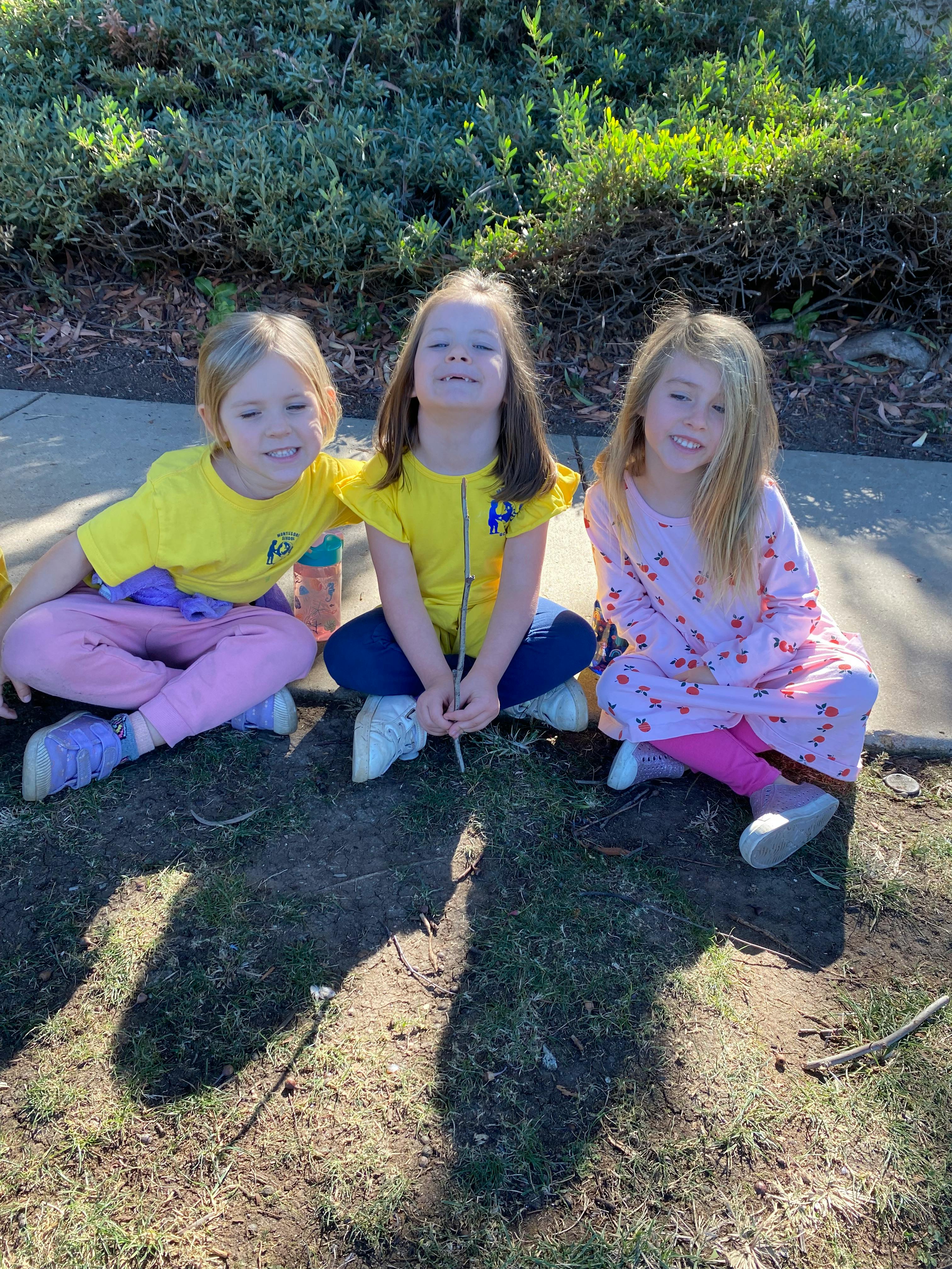 Three children sitting on the ground outdoors