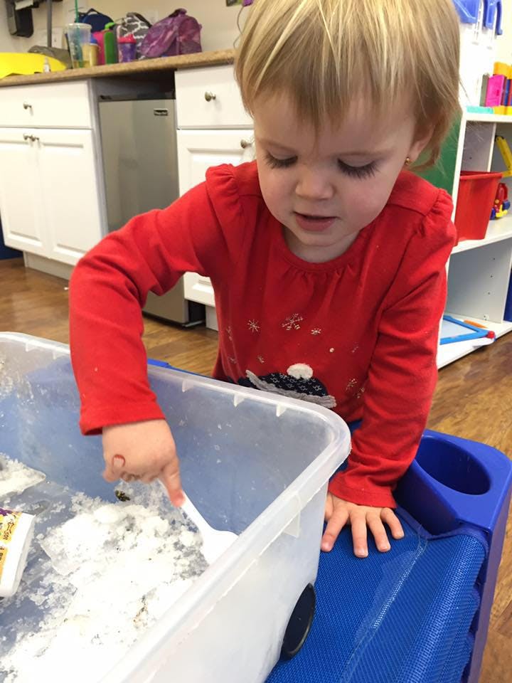 Child in red shirt playing with white powder in a clear bin