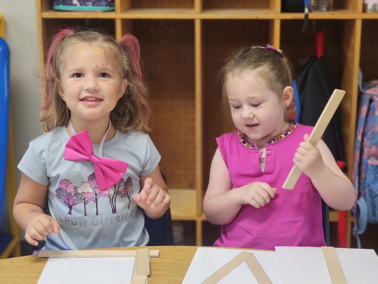 Two children at a table with craft sticks and building materials