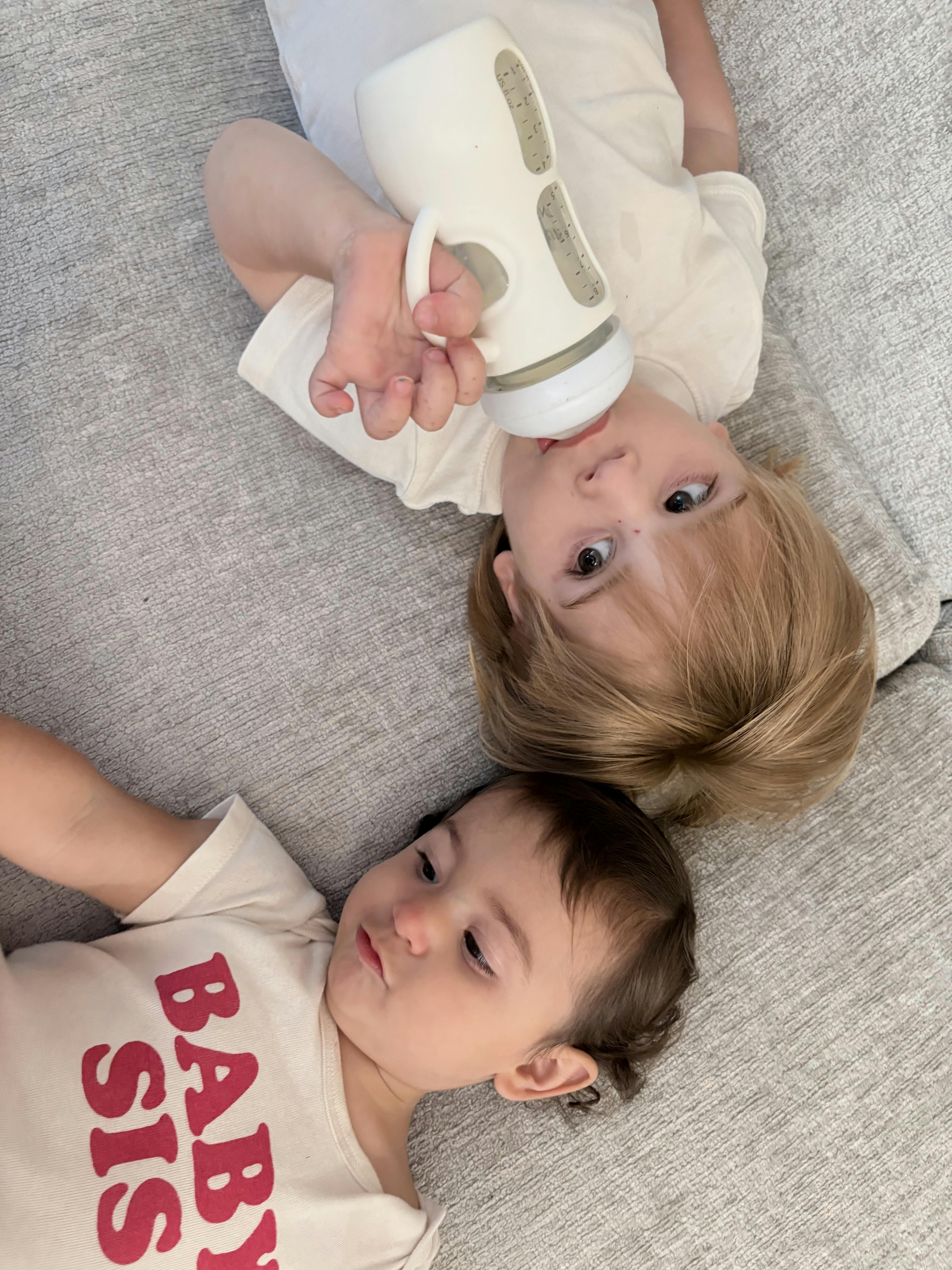Two children lying on a couch with one holding a baby bottle