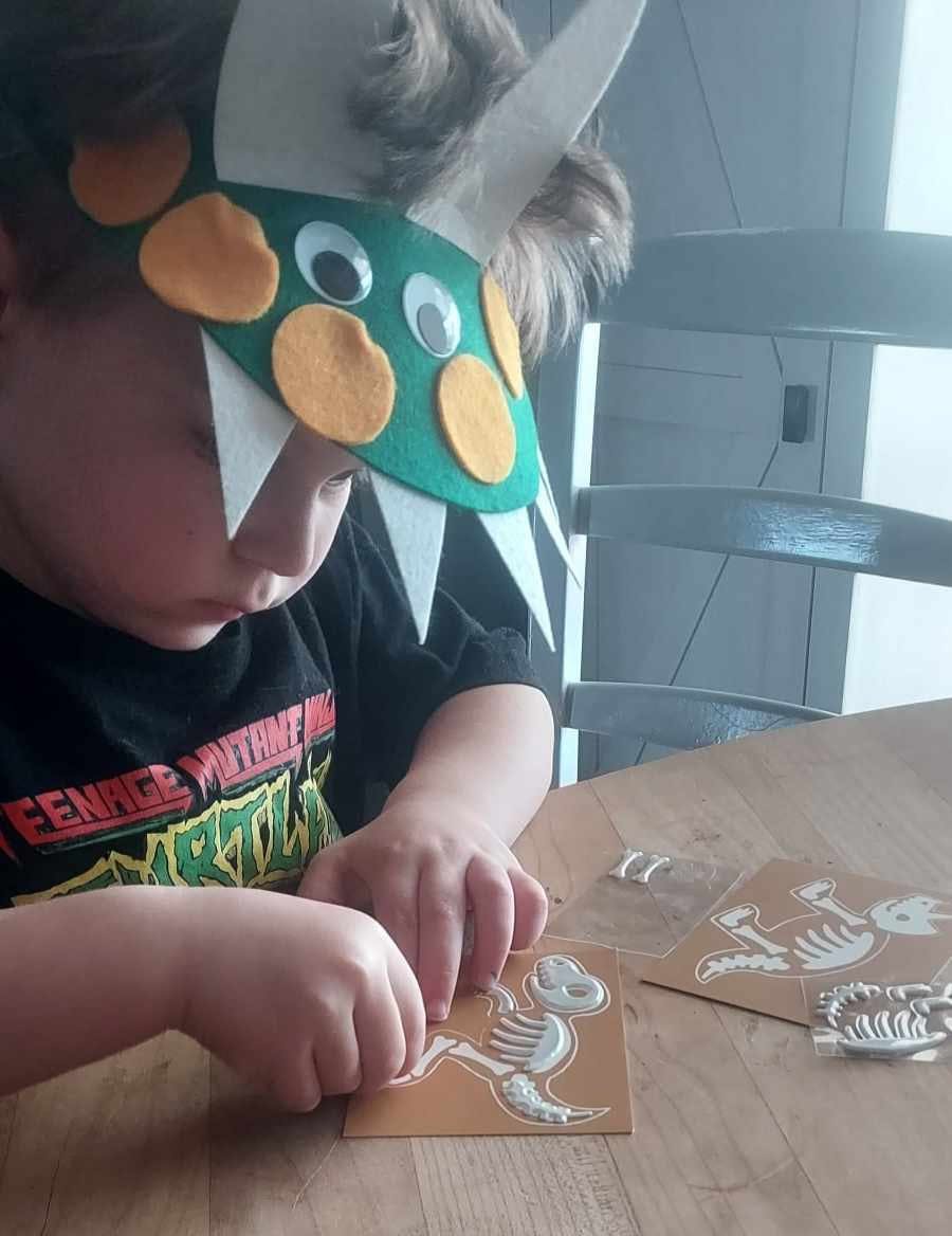Child wearing a dinosaur mask and working on a craft project
