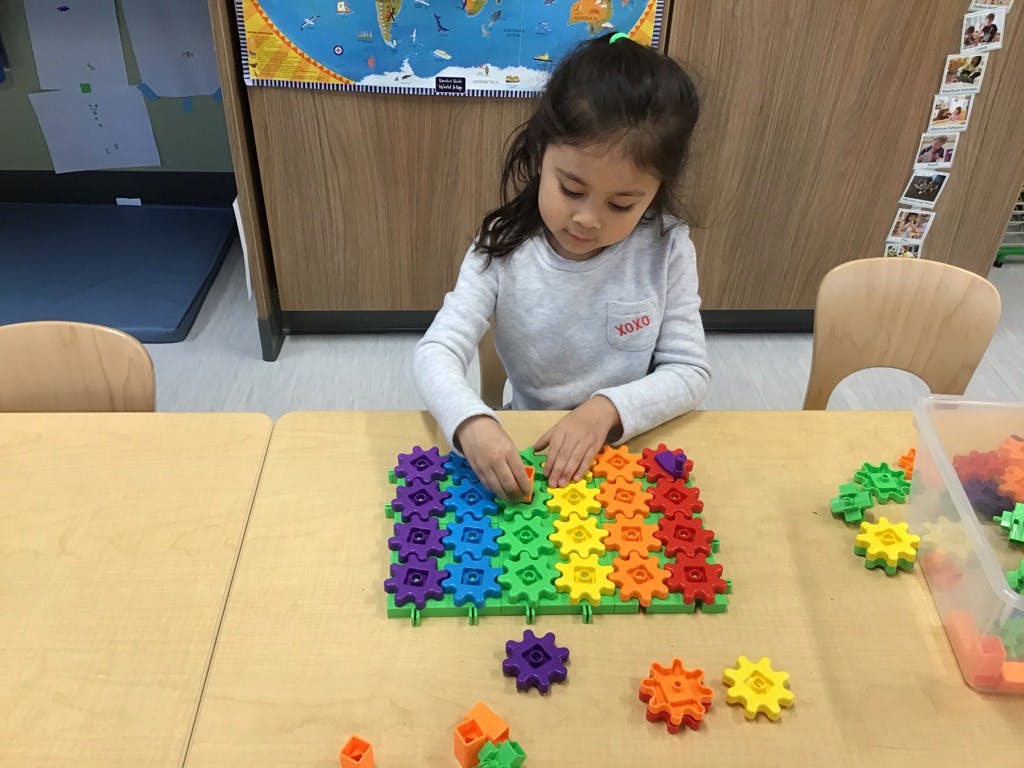 Child playing with colorful interlocking gears on a table in a classroom