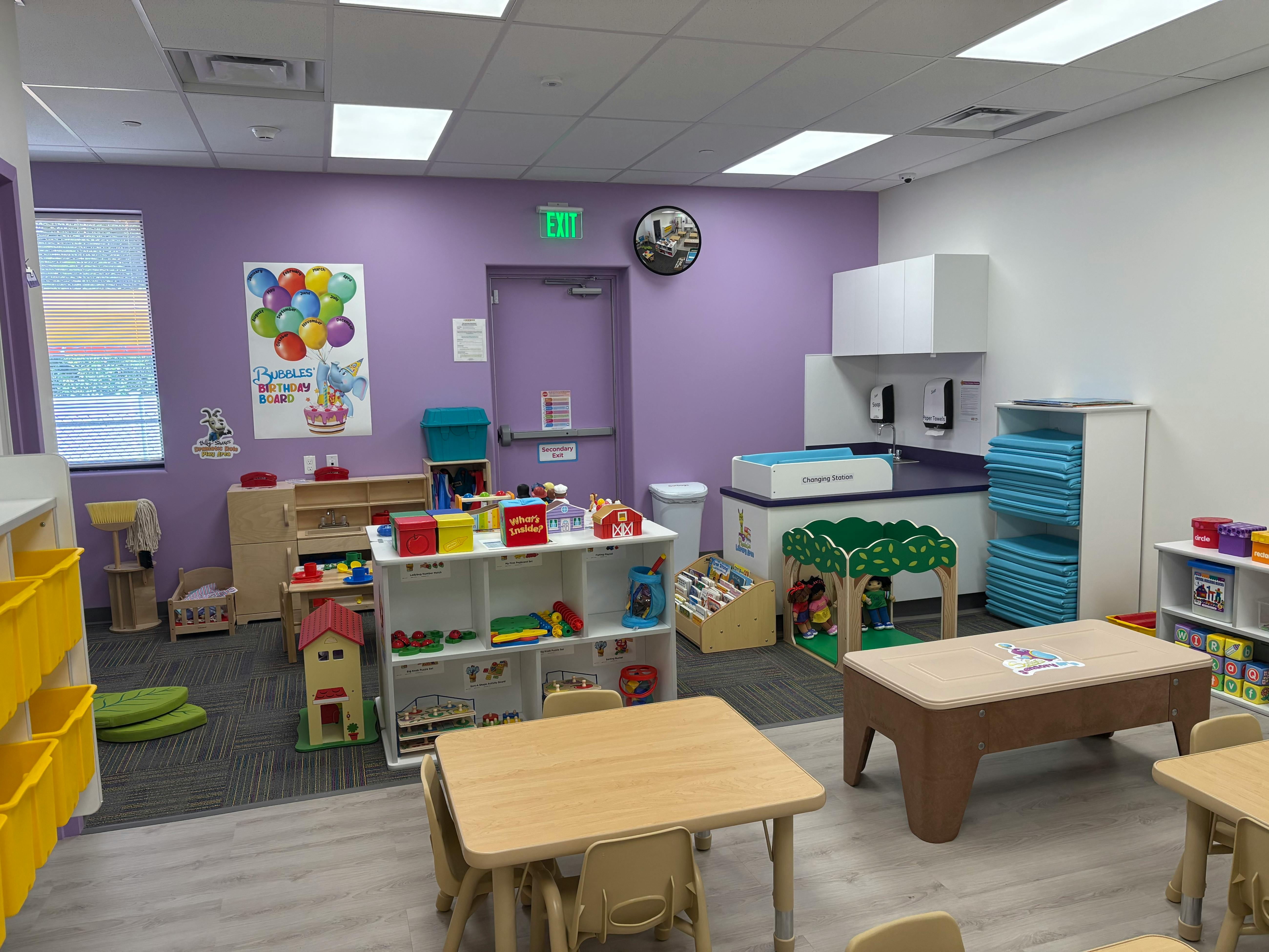 Playroom with small tables and chairs, shelves with toys, and a changing station