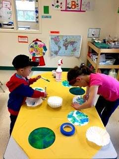 Two children doing an art project at a table in a classroom