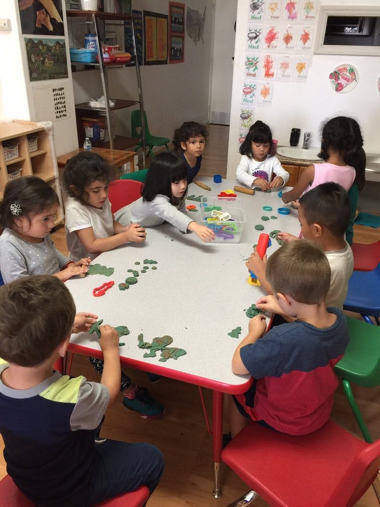 Children playing with modeling clay at a table in a classroom