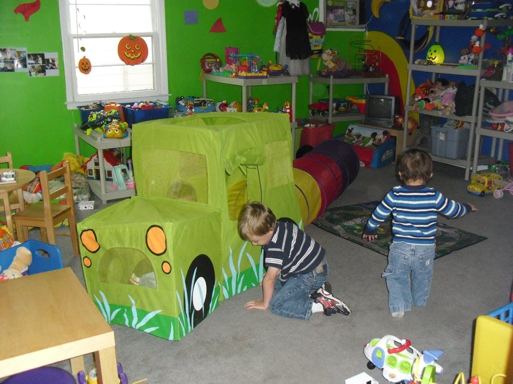 Two children playing with a green toy truck and tunnel in a playroom