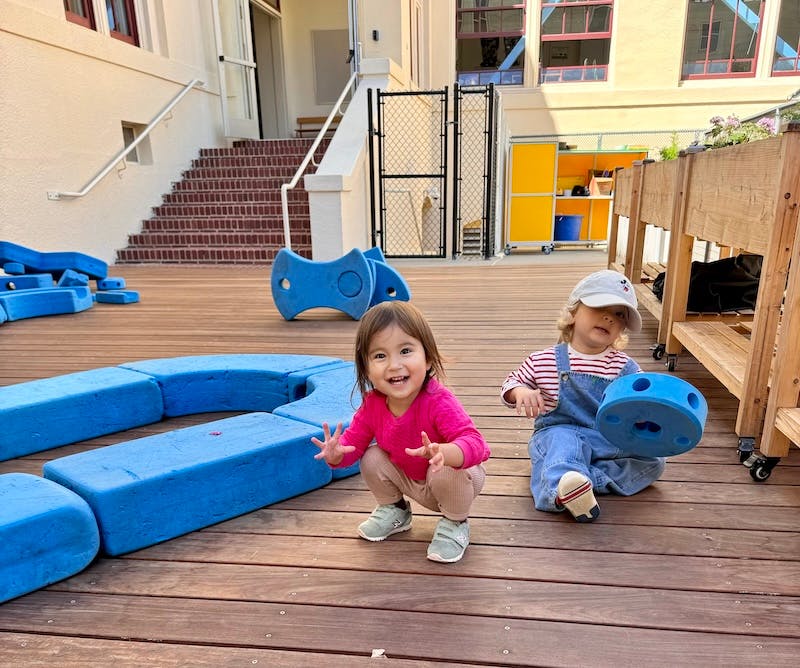 Two children playing with blue soft blocks on a wooden deck