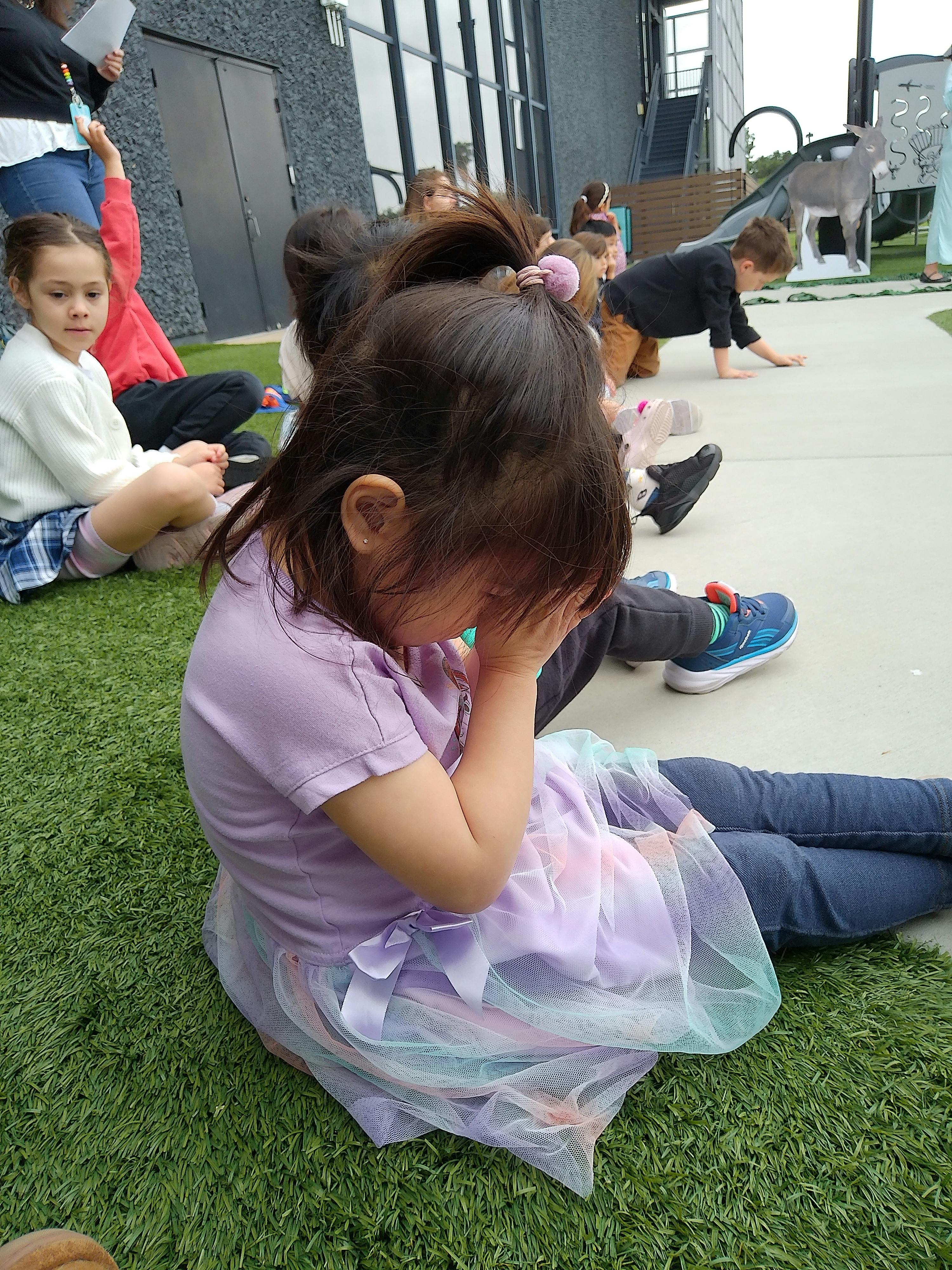 Child sitting on grass with hands covering face
