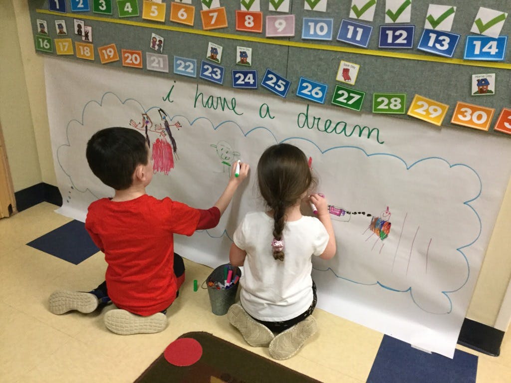 Two children drawing on a large paper with "I have a dream" written on it