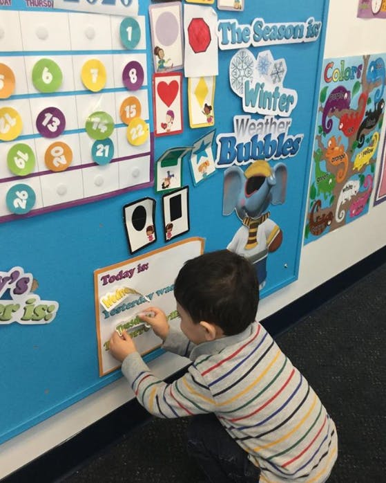 Child placing a sticker on a calendar board in a classroom