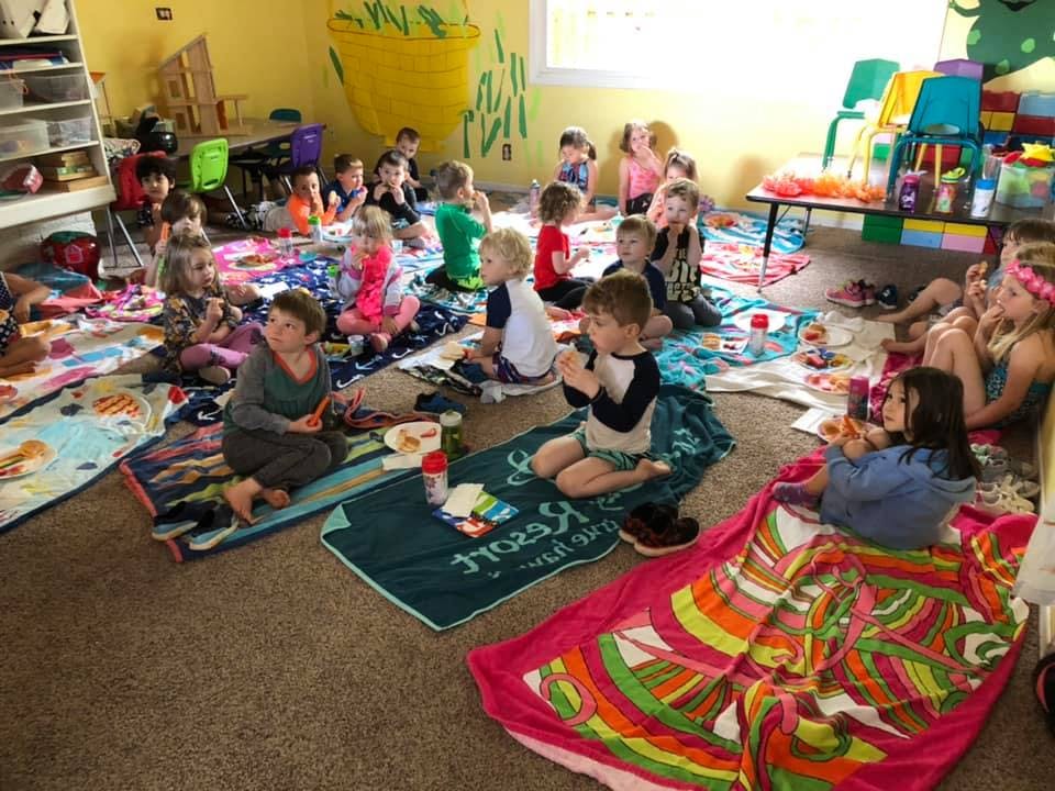 Many children sitting on blankets on the floor in a room