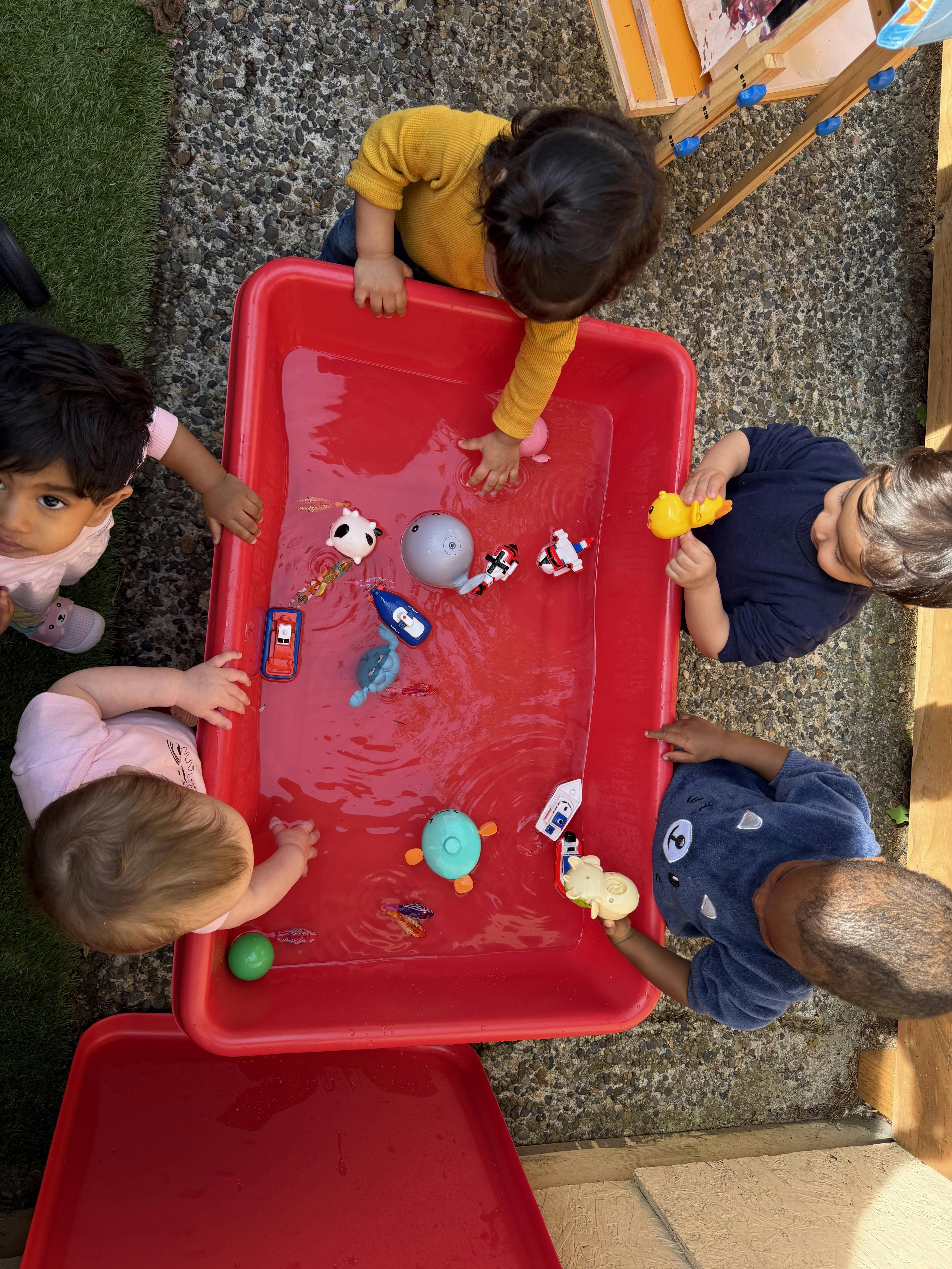Children playing with water and toys in a red tub