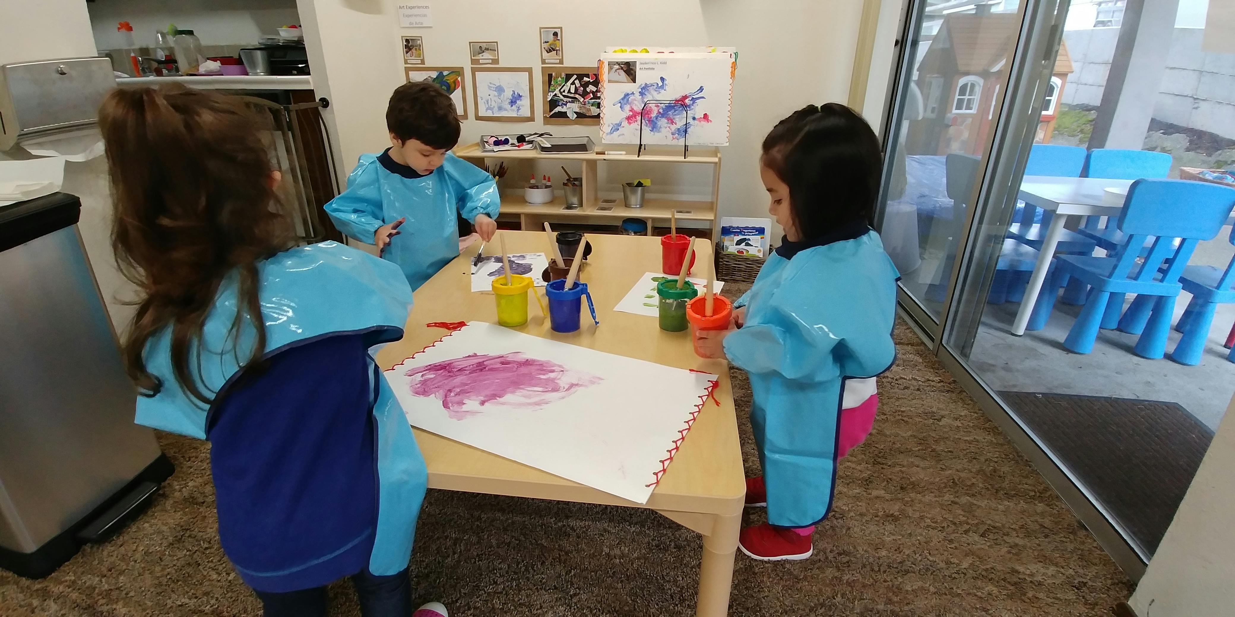 Three children painting at a table in a classroom